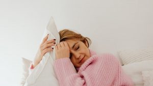 Woman peacefully resting with a cozy pink sweater and pillow, exuding calmness and relaxation.